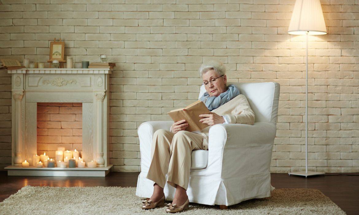 Donna anziana seduta su una poltrona classica, che potrebbe trovare solievo mediante l’ergonomia di un ausilio.